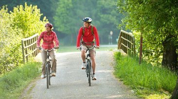 Paar fährt radelnd über eine Brücke in der Natur