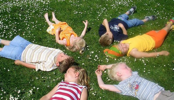 Sechs Kinder liegen entspannt auf einer blühenden Wiese
