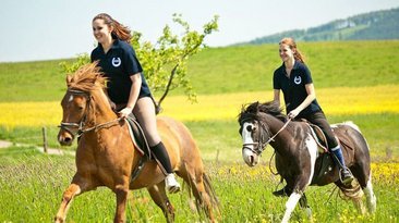Zwei Frauen reiten auf Pferden durch eine blühende Landschaft