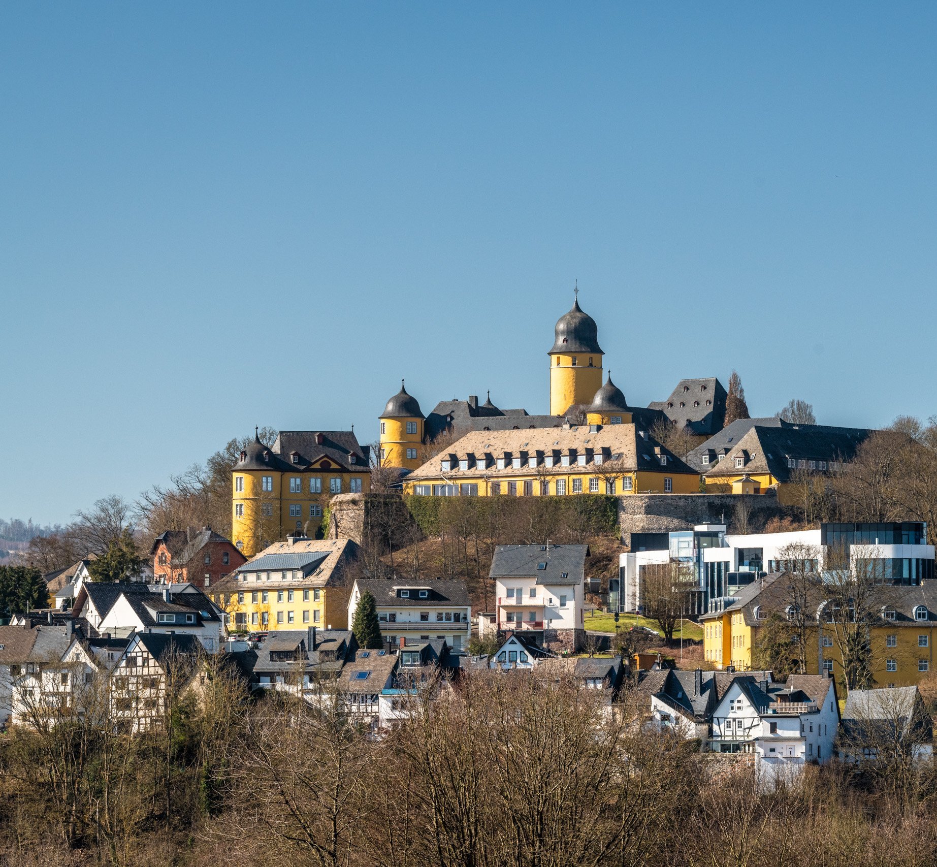 Eine Burg thront über einer Stadt mit gewöhnlicher Architektur im Vordergrund.
