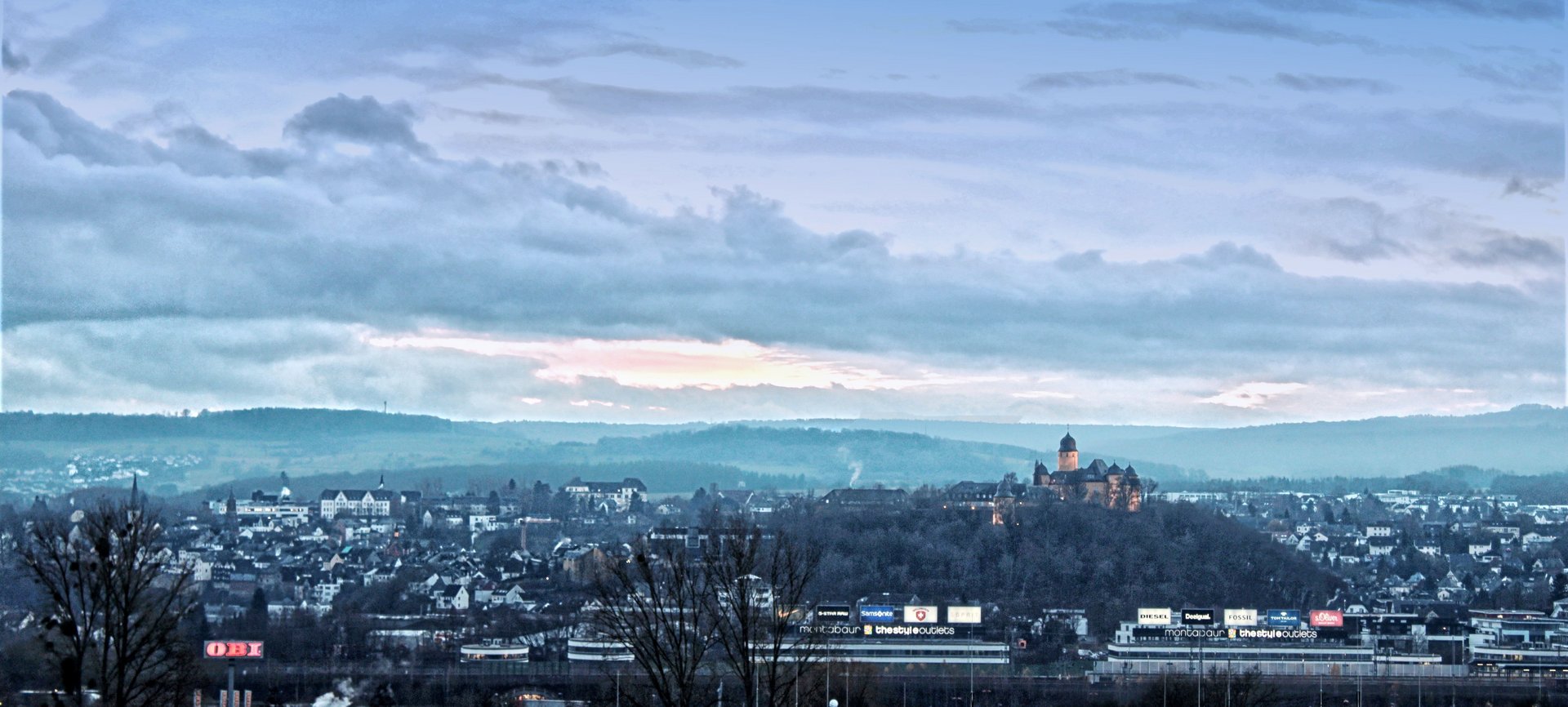 Blick auf eine Stadt mit Hügeln und Wolken am Himmel