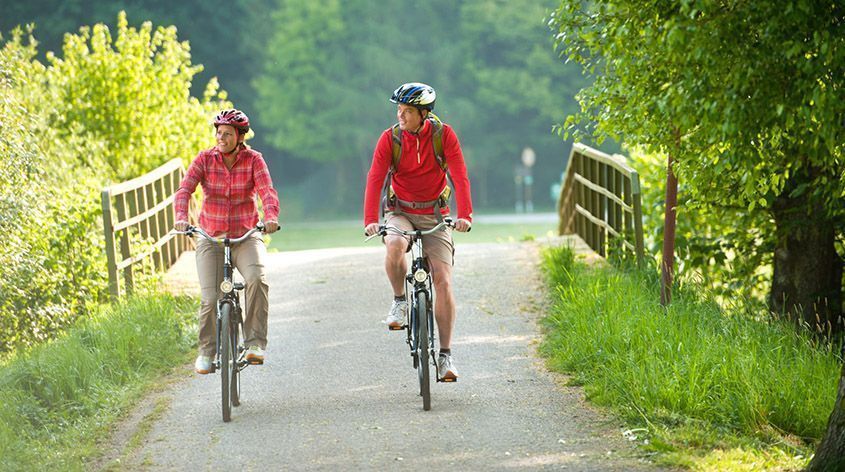 Paar fährt radelnd über eine Brücke in der Natur