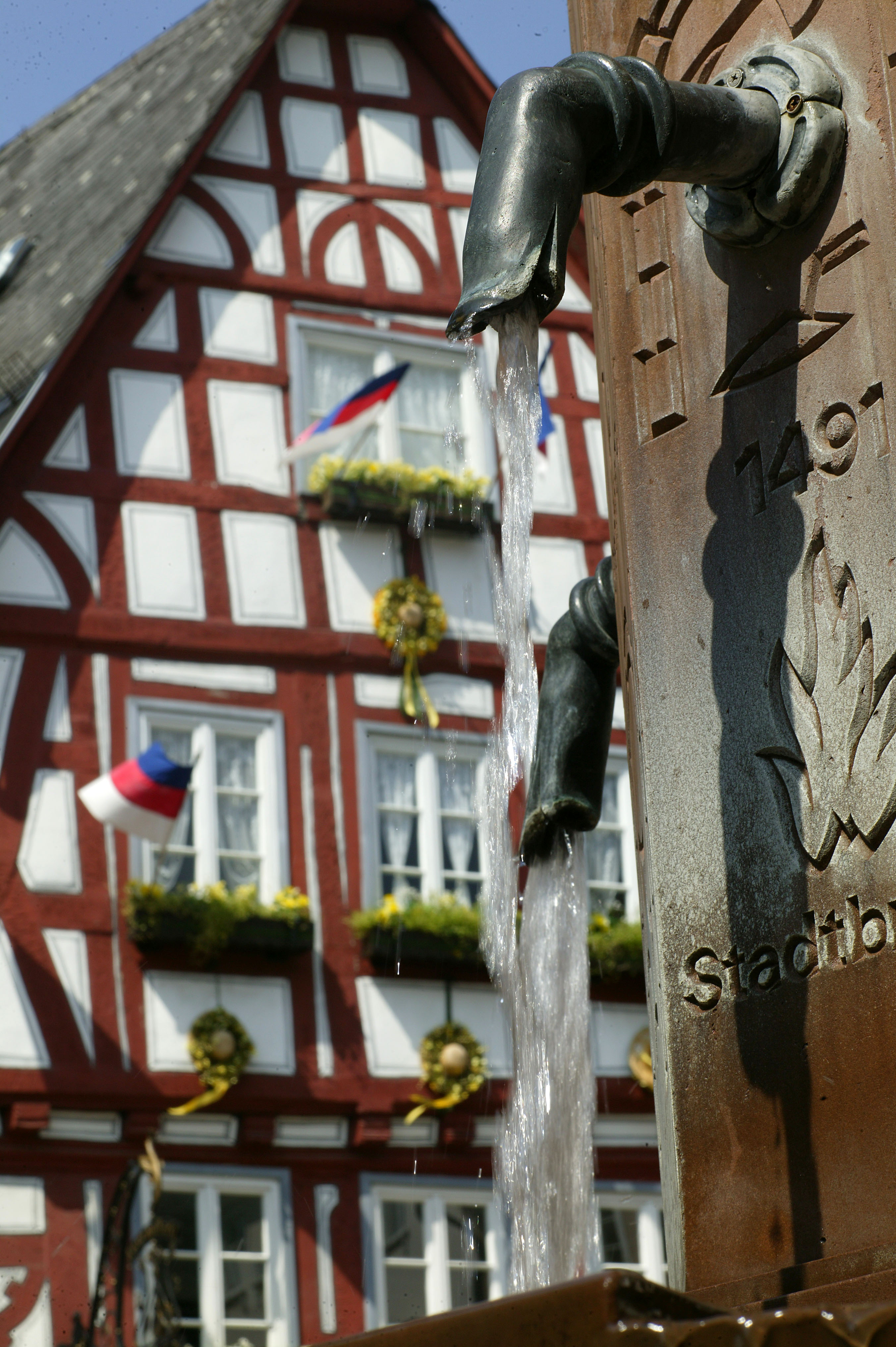 Wasserfontäne aus einem Brunnen vor einem bunten Fachwerkhaus