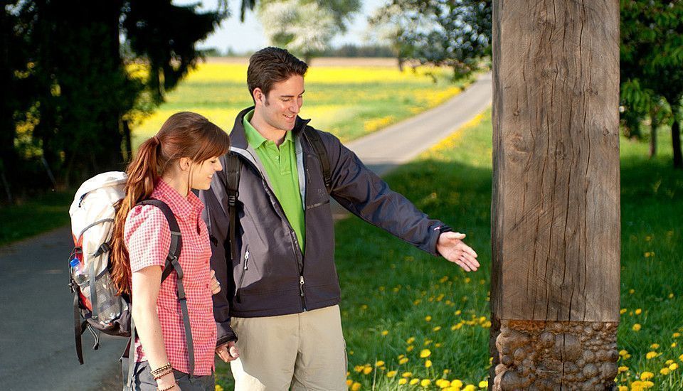 Pärchen am Wegweiser, umgeben von Blumen auf einem Wanderweg