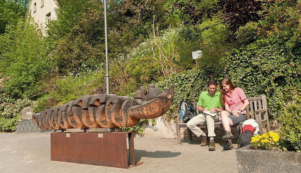Zwei Personen auf einer Bank neben einer großen Holzskulptur in der Natur