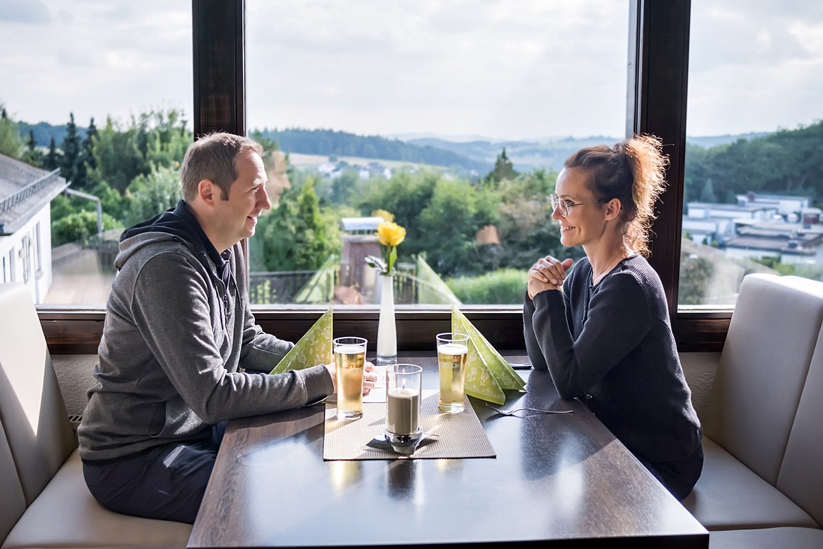 Zwei Personen sitzen am Tisch und genießen Getränke mit Blick auf die Landschaft